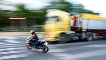 Motorcyclist passing in front of a large truck on a city street.
