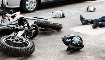 Crashed motorcycle and helmet lying on the road near an injured rider.