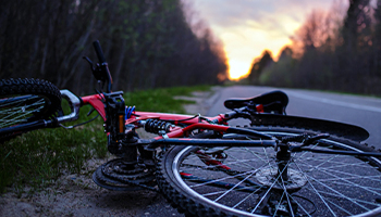 Two fallen bicycles on the side of a road at sunset.
