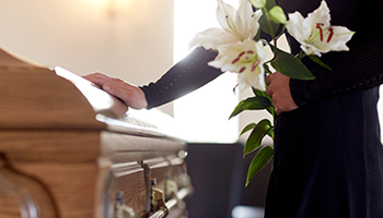 Mourner holding lilies and a program beside a casket at a funeral.